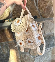 a hand holding a crocheted purse in front of a stone wall