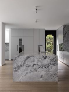 a large kitchen with marble counter tops and white cabinetry, along with an arched window