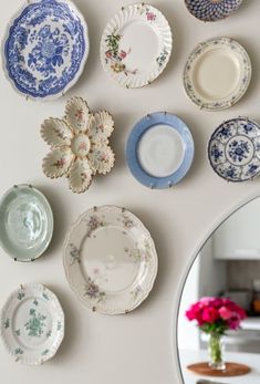 several plates are arranged on the wall in front of a mirror and vase with pink flowers