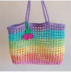 a crocheted bag hanging from a hook on a wall with a pink, blue, yellow and green handle