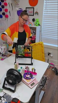 a woman in an orange and yellow jacket is working on some crafting supplies at a table