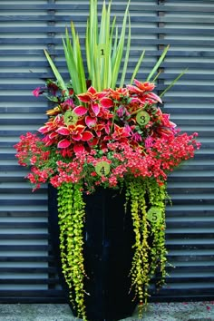 a large black vase filled with lots of red flowers and greenery next to a metal wall