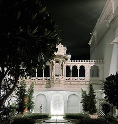 a white building with a fountain in front of it and trees around the courtyard at night