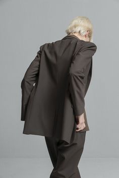 a woman with blonde hair wearing a black suit and heels standing in front of a gray wall