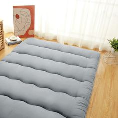 a large mattress is on the floor in front of a wooden table with a plant