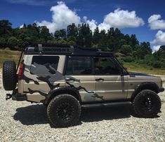 an suv with camouflage paint parked on gravel