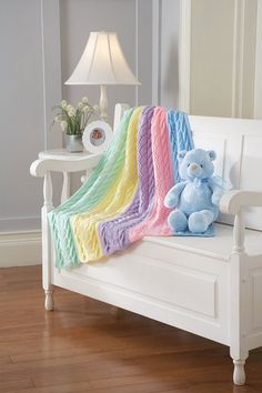 a teddy bear is sitting on a white bench with a colorful blanket draped over it