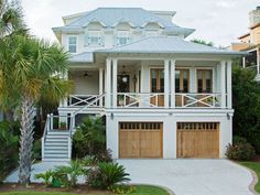 a large white house with two garages on the front and second story, surrounded by palm trees