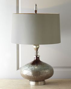 a table lamp with a white shade on it and a wooden surface in front of a window