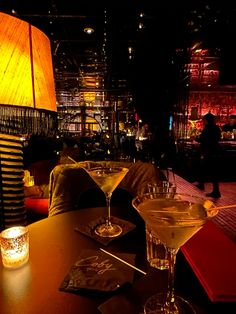 two martini glasses sitting on top of a wooden table next to a lit up lamp