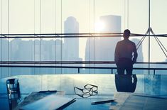 a man standing in an office looking out the window at his work space and skyscrapers