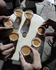 several people sitting around a table with cups of coffee in front of them and their hands on the tray