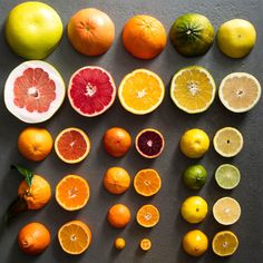 various citrus fruits are arranged on a gray surface, including grapefruits, oranges and lemons