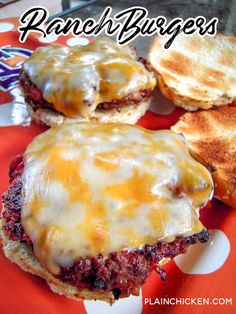 three hamburgers with cheese on them sitting on a red plate next to some bread