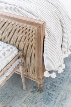 the bed is made with wicker and white linens on it, along with a blue rug