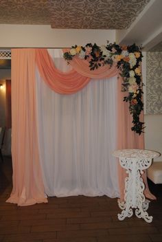 a white table with flowers on it in front of a pink and orange drape