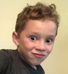 a young boy with curly hair is smiling at the camera and has an odd look on his face