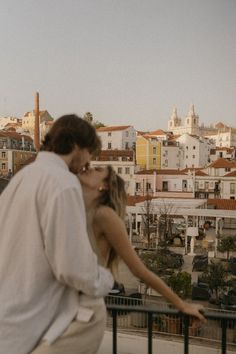 a man and woman kissing while standing next to each other on top of a balcony