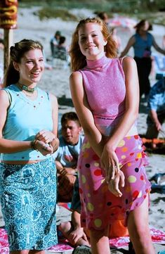 two women standing on the beach with people in the background