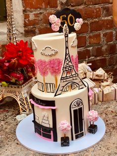 a three tiered cake is decorated with pink flowers and the eiffel tower