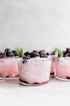 three dessert cups filled with berries and topped with rosemary sprigs on a white surface