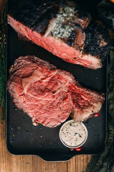 two steaks sitting on top of a black tray next to some seasoning and pepper