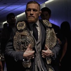 a man in a suit and tie holding up two gold wrestling belts while standing next to other men