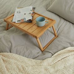 a wooden tray with a cup on top of it next to a pillow and blanket