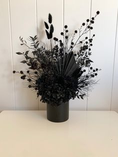 a vase filled with lots of black flowers on top of a white table next to a wall