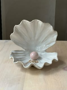 a white shell shaped bowl with a pink bead in the center on a wooden table