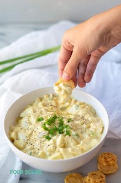 a person dipping some kind of food into a bowl with crackers on the side