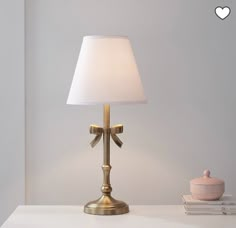 a lamp that is on top of a white table next to a book and cup