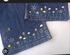 two pieces of denim with embroidered flowers and bees on the side, sitting next to each other