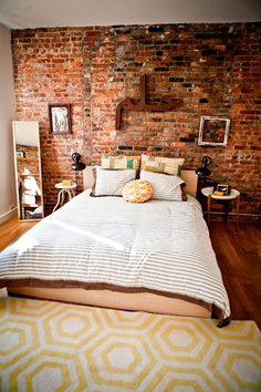 a bedroom with brick walls and white bedding in front of a yellow rug on the floor