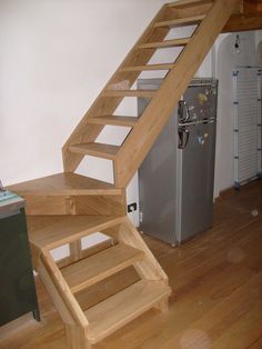 a wooden stair case next to a refrigerator in a room with hard wood flooring