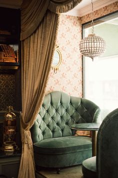 a green chair sitting in front of a window next to a table with a lamp on it