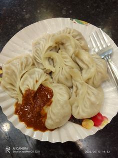 some dumplings are on a paper plate with sauce and a fork next to it