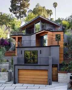 a two story house with wooden garage doors and windows on the second floor, surrounded by greenery