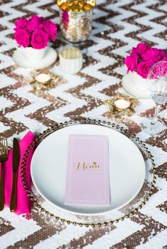 a place setting with pink napkins and silverware on a tableclothed table