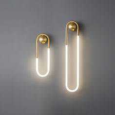 two lights that are next to each other on a gray wall, one is gold and the other is white