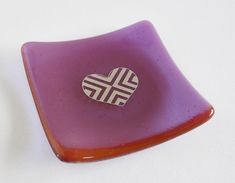 a purple glass plate with a heart shaped sticker on the front and bottom, sitting on a white surface