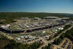 an aerial view of a race track with cars parked in the lot and trees surrounding it