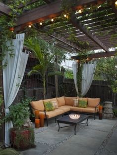 an outdoor living area with couches, tables and lights hanging from the pergolated roof