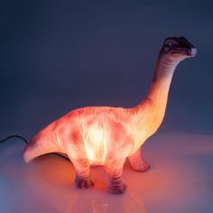 an illuminated toy dinosaur standing on a white surface with its head turned to the side