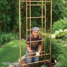 a woman kneeling down in front of a garden trellis