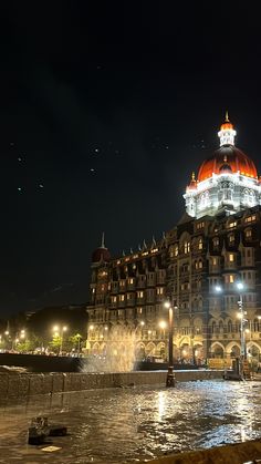 a large building lit up at night with lights on it's roof and water fountain in the foreground