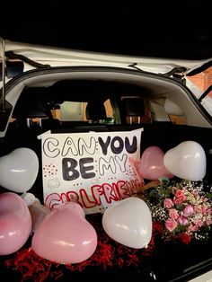 a car with balloons and flowers in the trunk, next to a sign that says can you be my girlfriend?