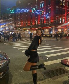 a woman in short skirt and boots standing on the street with her legs spread out