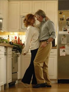 a man and woman standing in a kitchen next to each other with their arms around each other