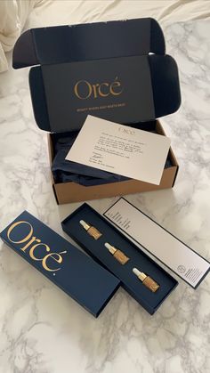 an open box with two pairs of earrings in it on a marble counter top next to other boxes